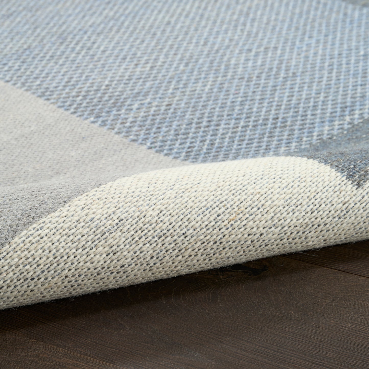 Blue & beige patchwork woven area rug, folded corner showing textured weave on dark wooden floor.