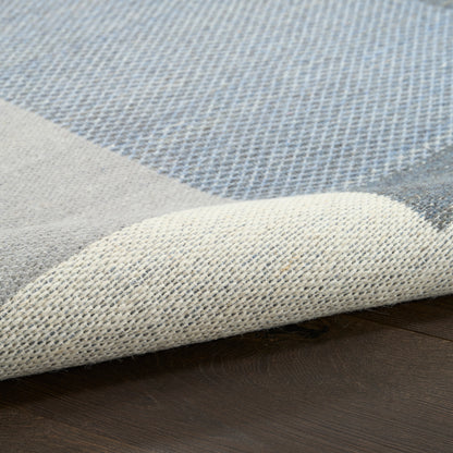 Blue & beige patchwork woven area rug, folded corner showing textured weave on dark wooden floor.