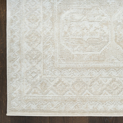 Ivory textured area rug with subtle geometric medallion and border patterns on dark wood floor.