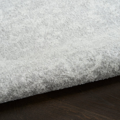 Close-up of a light gray round shag rug edge resting on dark wood floor, plush soft pile.
