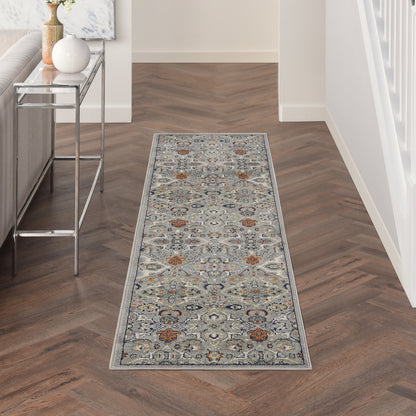 Long narrow Persian-inspired gray-blue hallway runner with orange motifs on a dark wood herringbone floor.