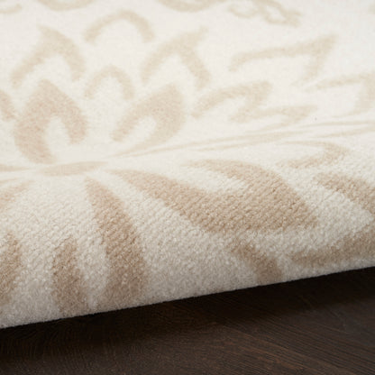 Cream-beige patterned area rug with soft plush pile, featuring leaf-like motifs on a dark wood floor.