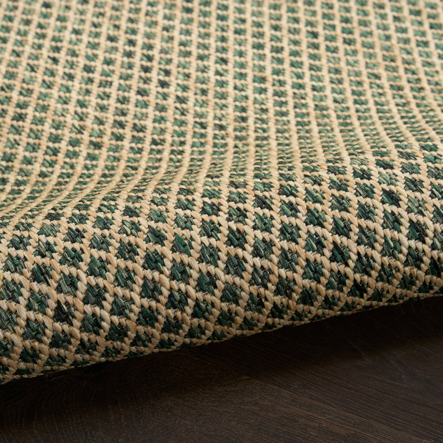 Beige and green woven rug with geometric diamond pattern, natural fiber texture, laid on dark wood floor.