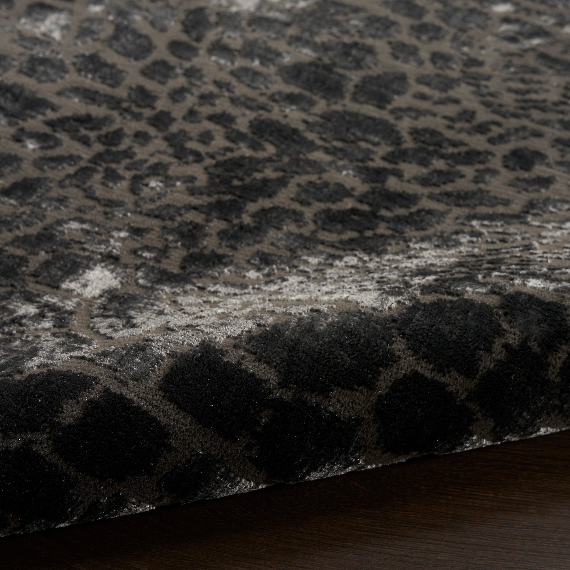 Close-up of a plush leopard-print rug in charcoal gray with black spots, laid on dark wood floor.