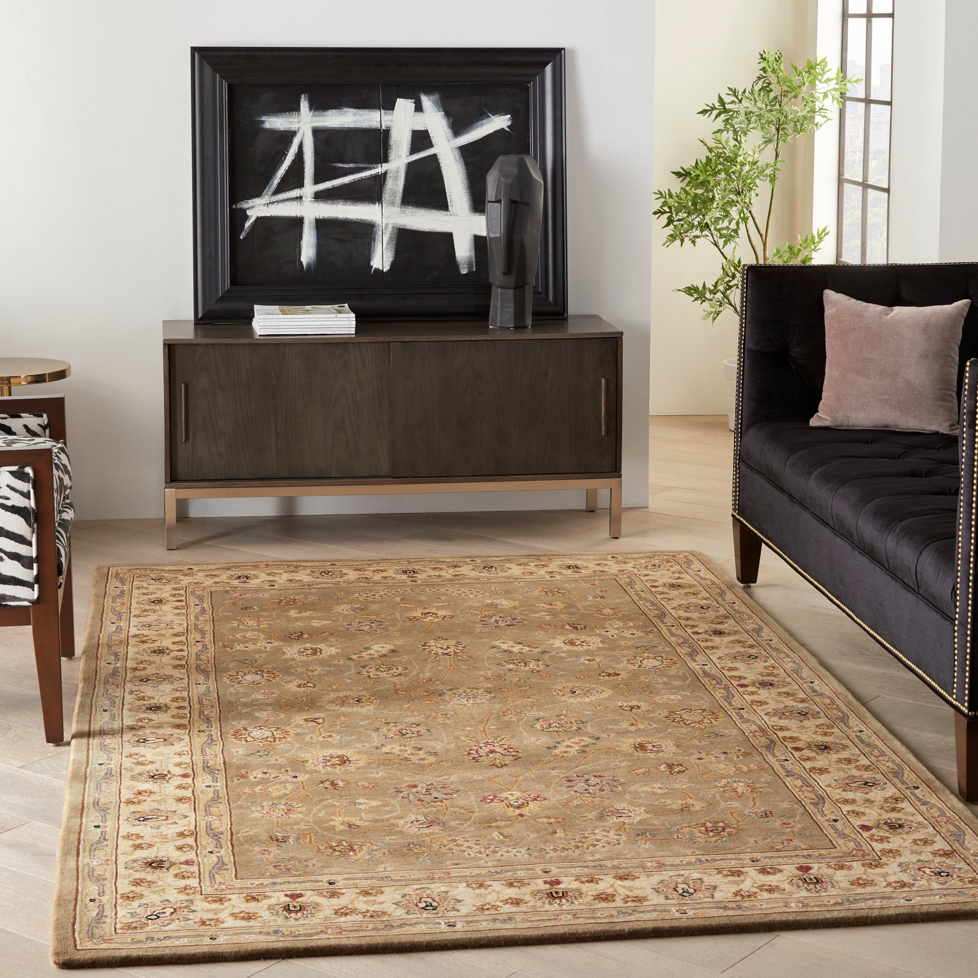 Living room with beige oriental rug, dark wood console, abstract black-and-white art, plant, and tufted black sofa.
