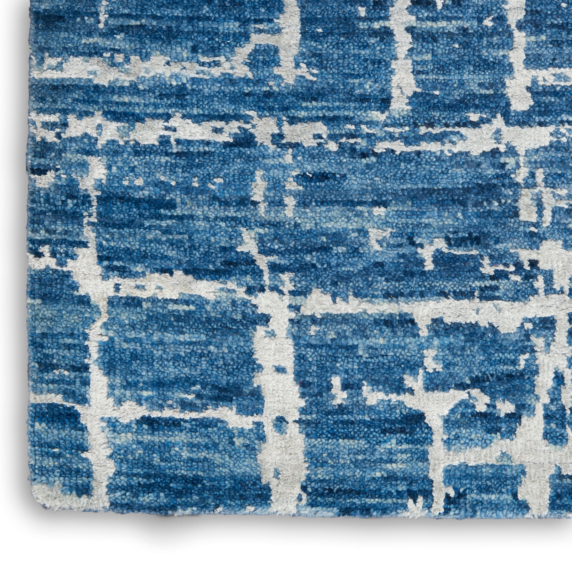 Blue rug with white geometric grid pattern, textured pile, cropped edge with fringe.