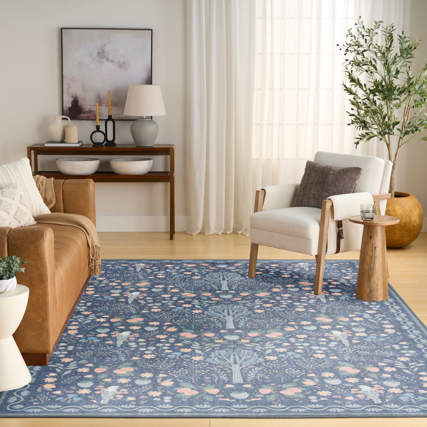 Blue patterned area rug with floral motifs in a living room featuring a leather sofa, beige armchair, and wooden console.