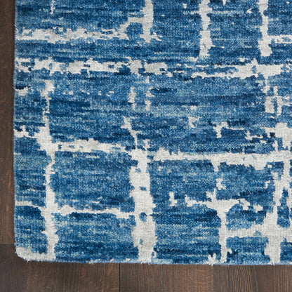 Textured blue area rug with white geometric grid pattern on dark wood floor.