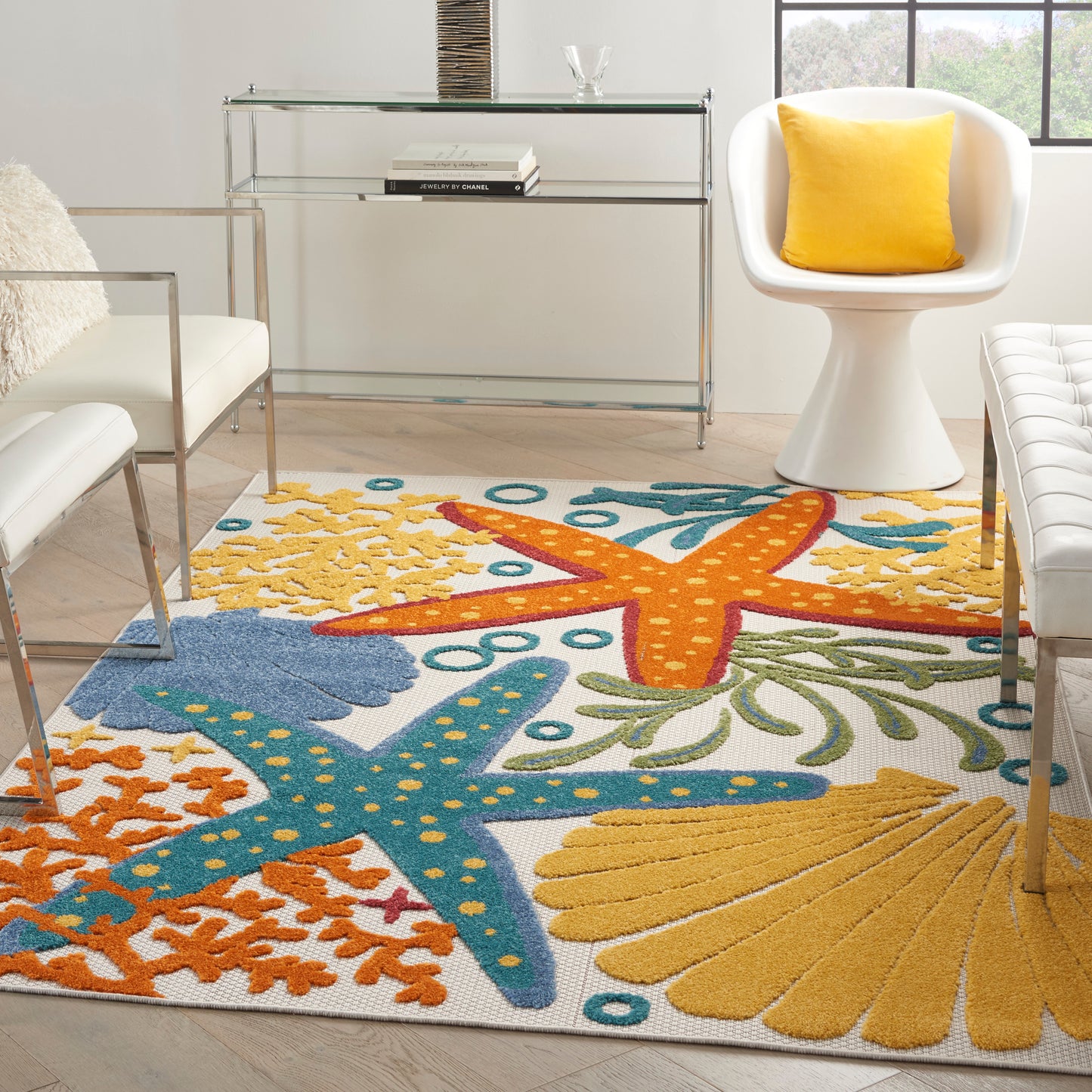 Coastal living room with a bright sea-pattern rug featuring starfish and coral in yellow, orange and blue, with white modern chairs.