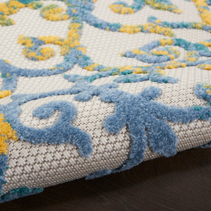 Close-up of a cream outdoor rug with blue and yellow ornate scroll pattern and soft tufted pile.