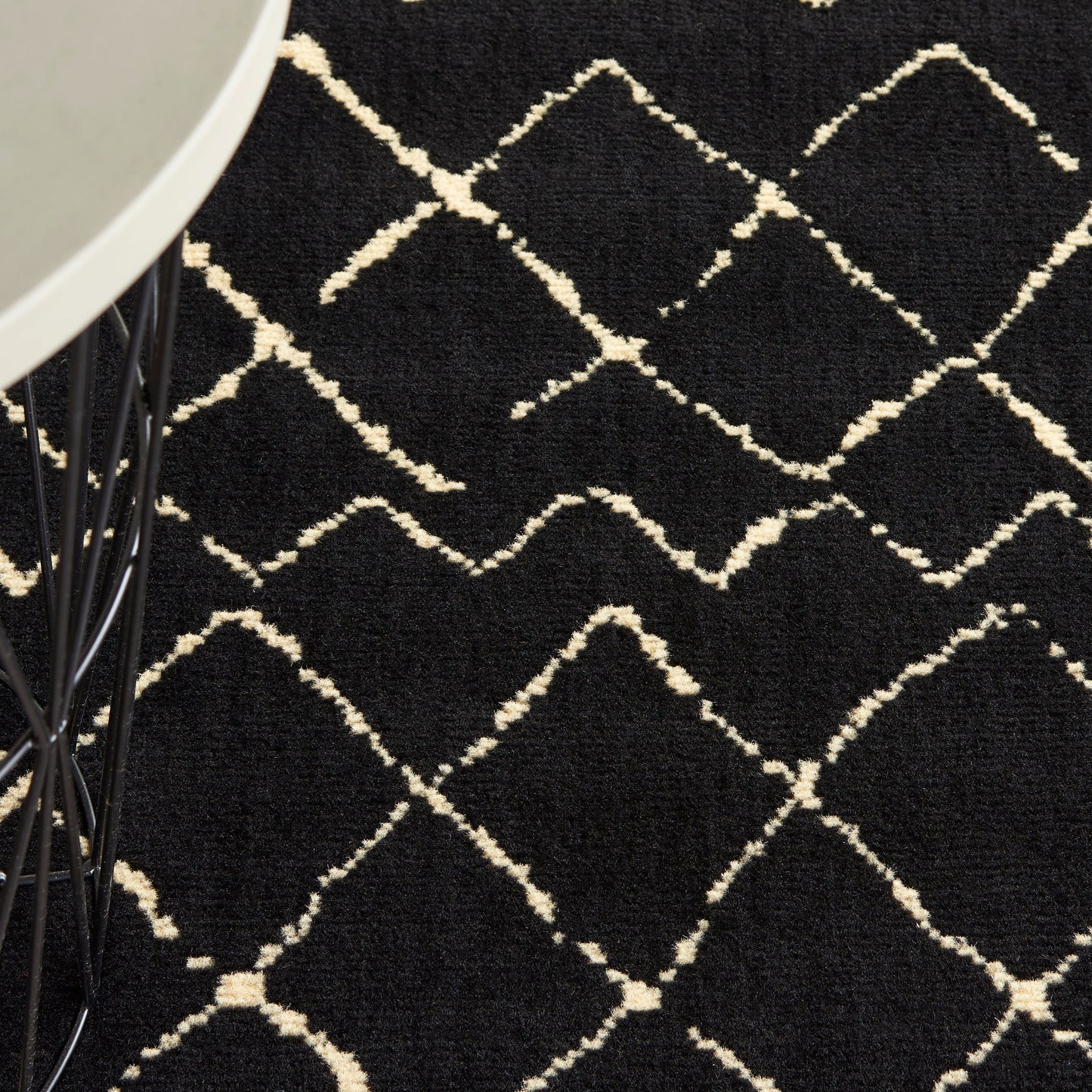 Black area rug with cream diamond lattice pattern; plush pile near a round table with black wire legs.