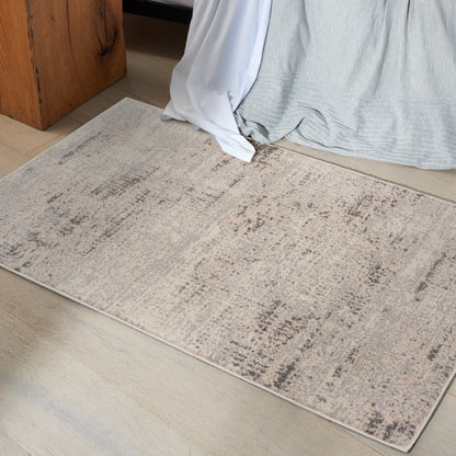 Neutral beige rectangular area rug with a subtle distressed taupe pattern on a light wood floor beside a bed.