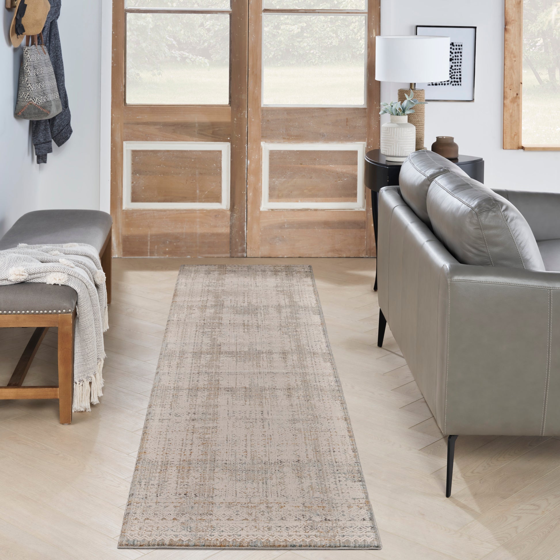 Neutral beige distressed runner rug in a cozy living room with a gray sofa, bench, and wooden doors.