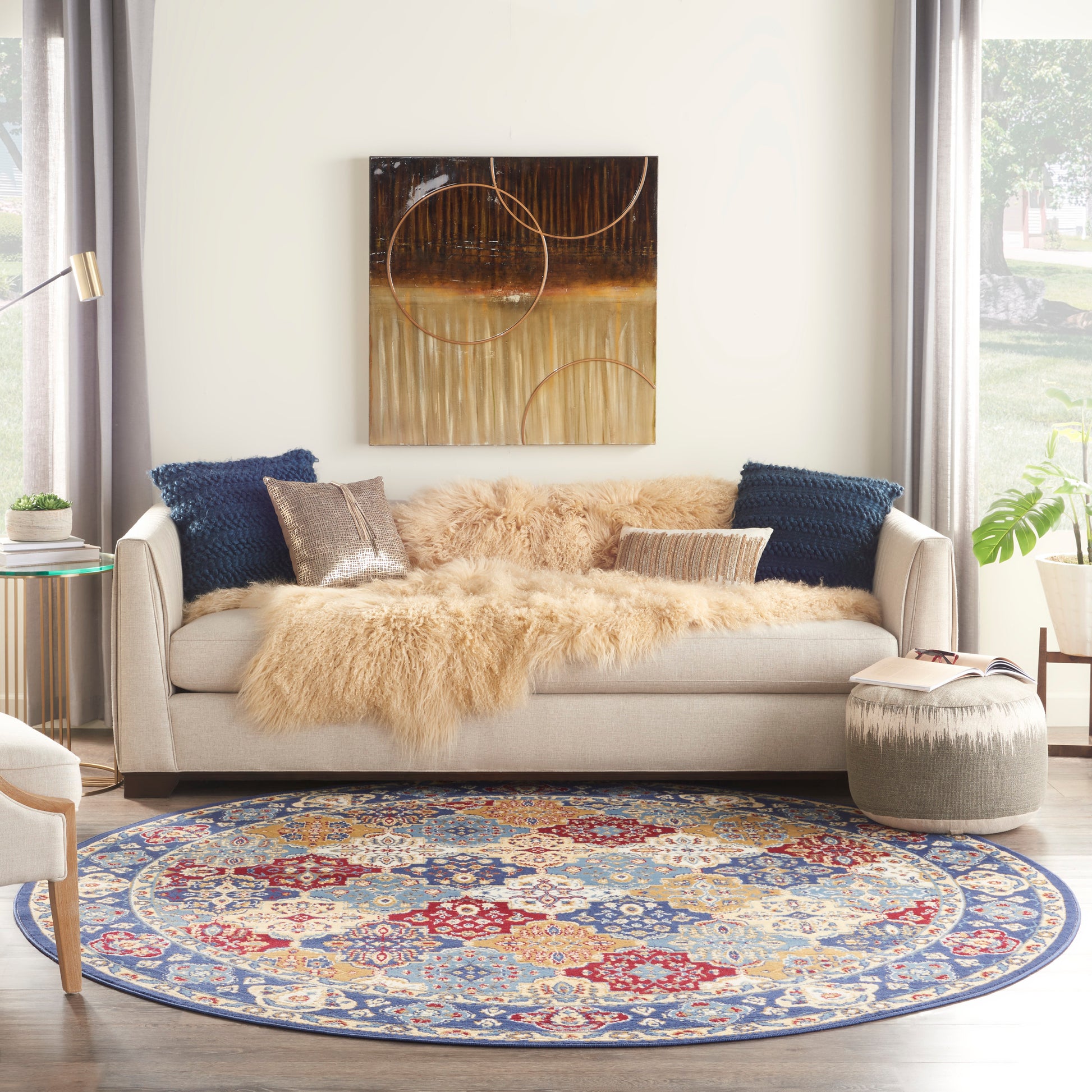 Beige sofa with fur throw and navy cushions, circular abstract art, round blue-red-gold patterned rug; cozy living room.