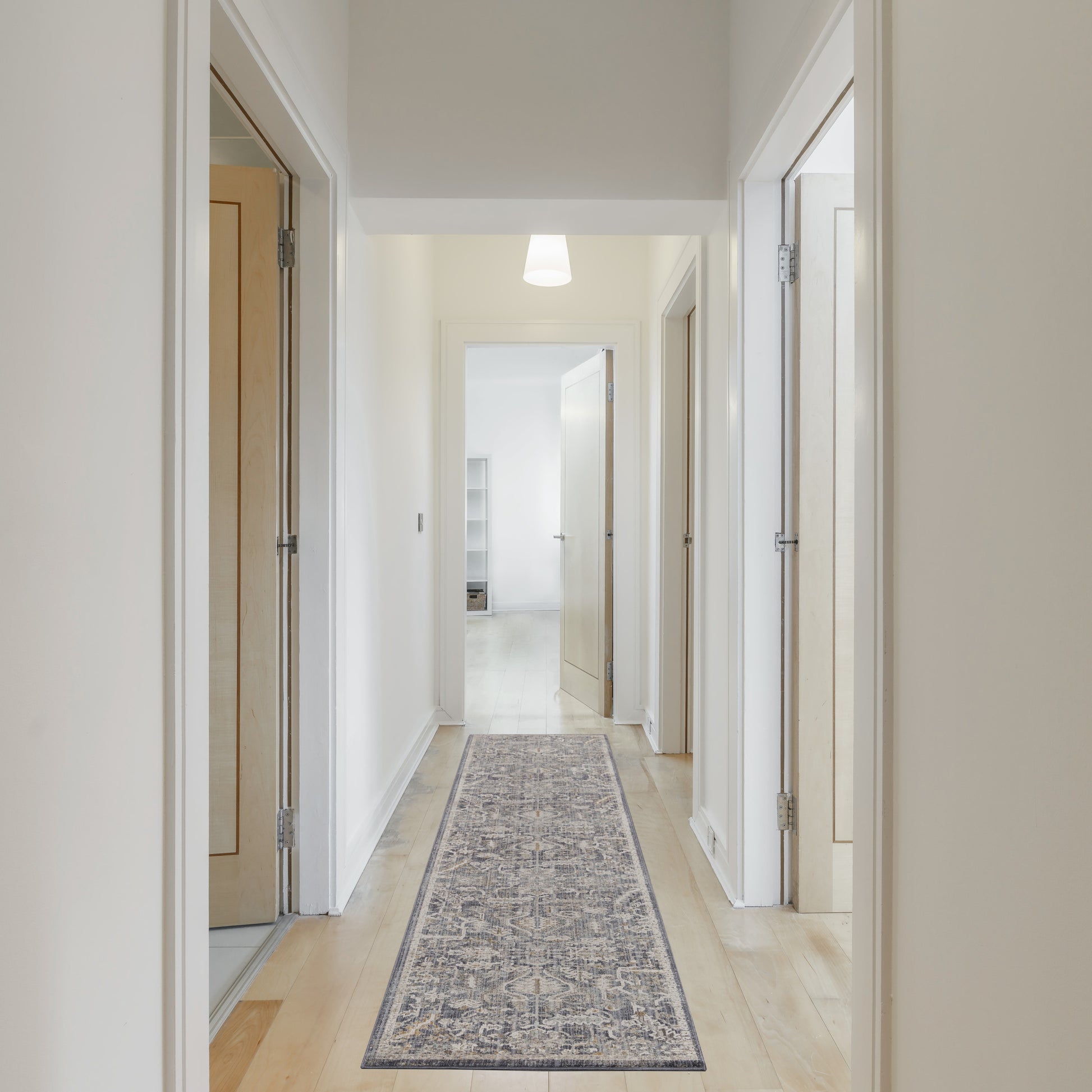 Bright hallway with white walls, light wood doors, pale wood floor, blue-gray patterned runner rug.