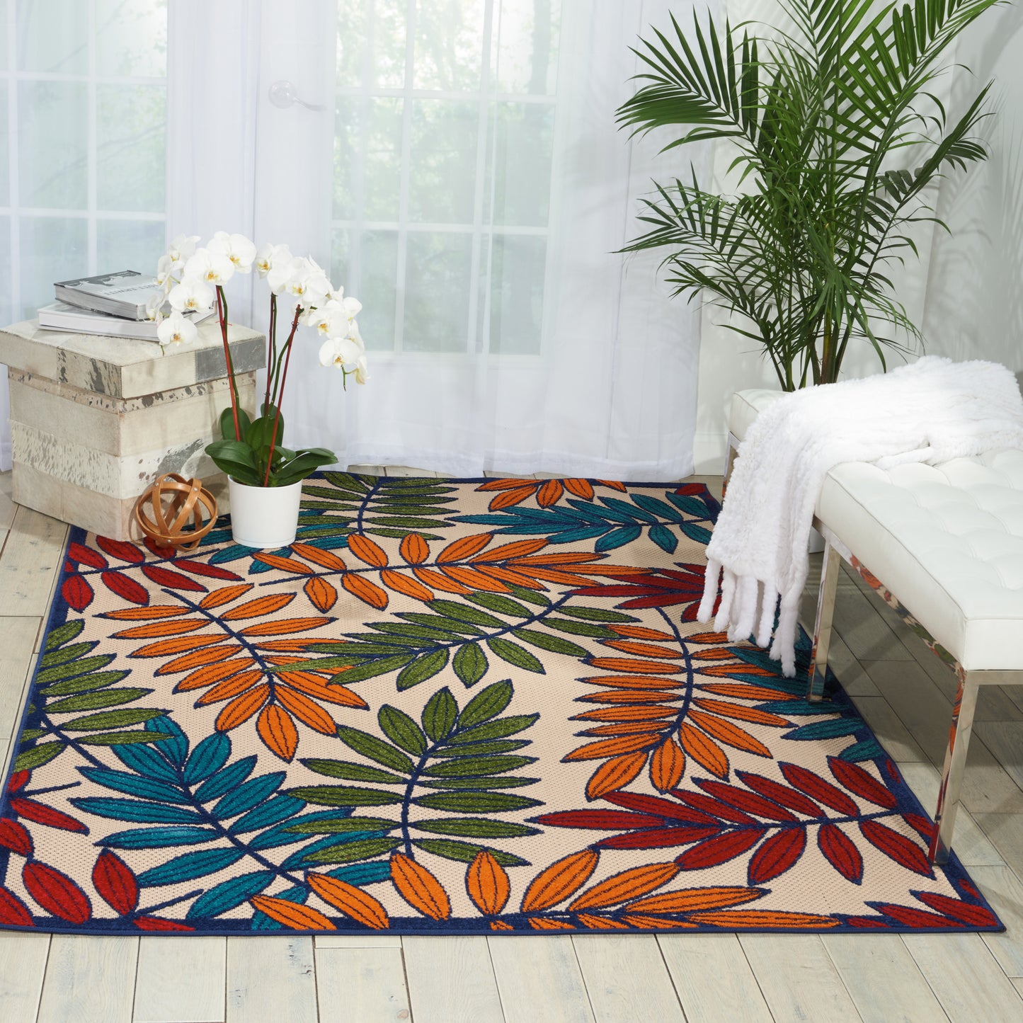 Colorful leaf-pattern area rug with blue, orange, green and red leaves on cream in a bright living room.