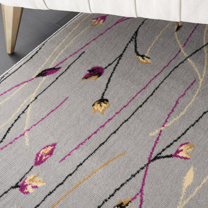 Light gray rug with slender black, magenta and gold floral lines and buds, under a beige sofa.