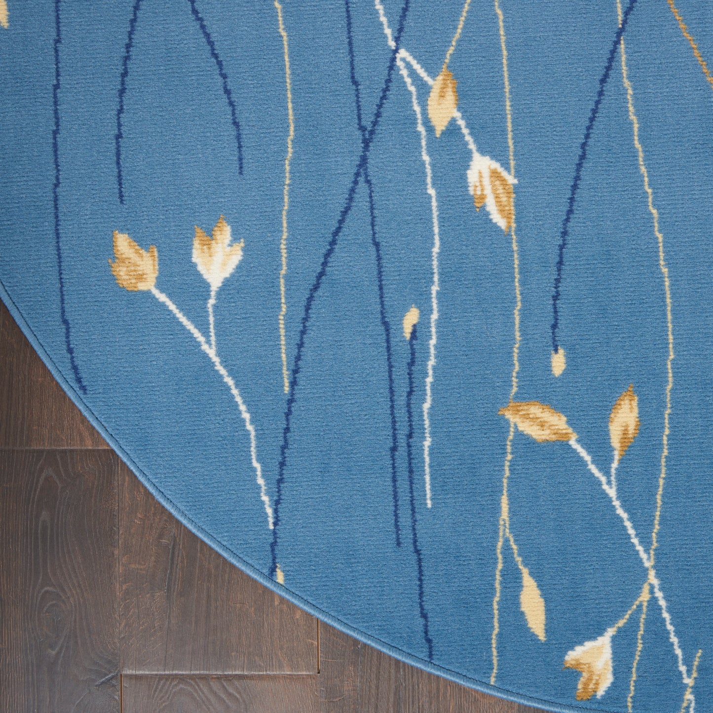 Round blue area rug with abstract white and navy stems and yellow leaf accents.