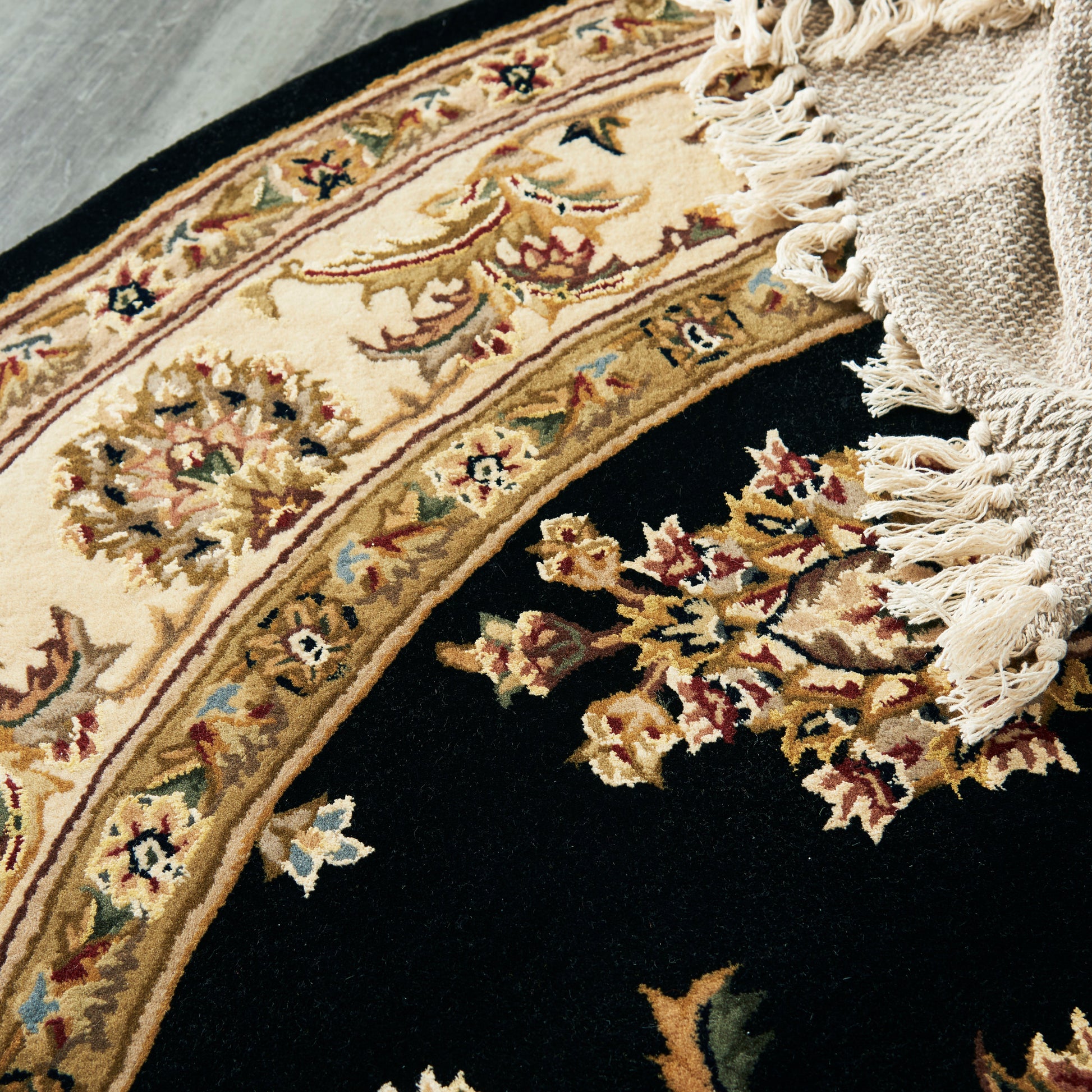 Ornate oriental rug with ivory border and floral medallions on black field, fringed cream tassels.