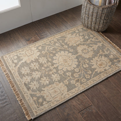 Beige & cream floral pattern area rug with fringed borders on dark wood floor by a wicker basket.