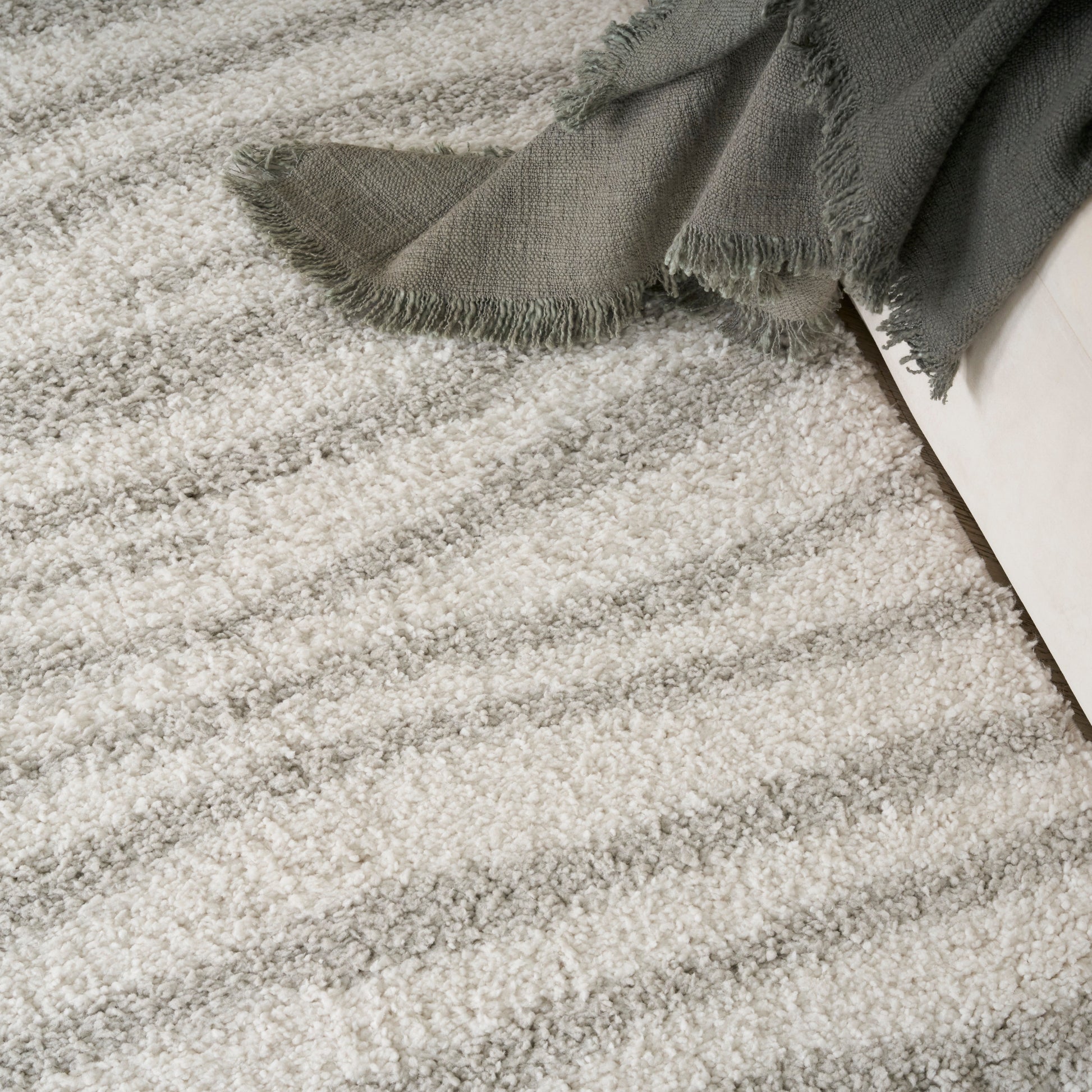 Cream shag rug with plush pile & gray fringed blanket draped over a white sofa.