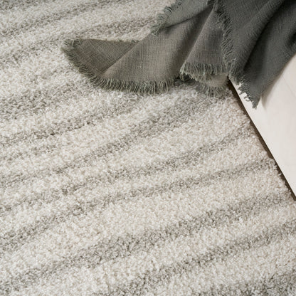 Cream shag rug with plush pile & gray fringed blanket draped over a white sofa.