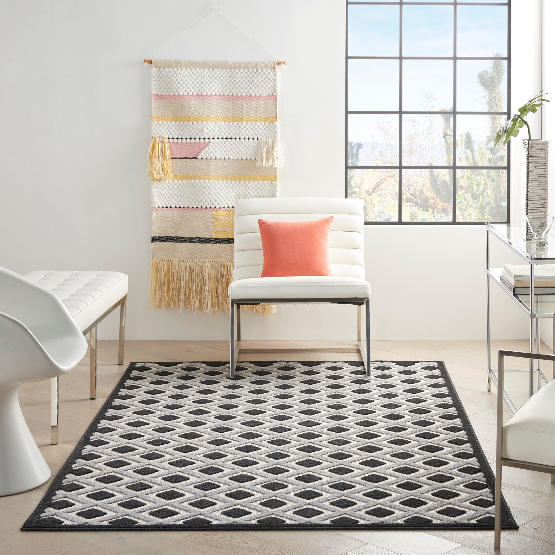 Black-and-white diamond patterned rug in a bright modern living room with a white chair and coral pillow.