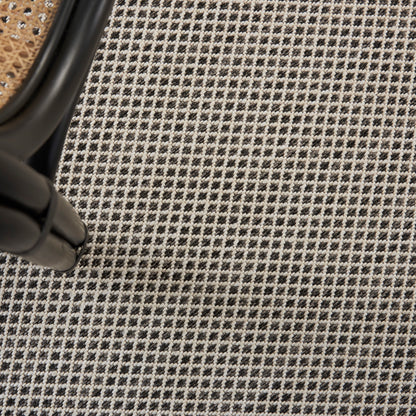 Black metal chair leg with curved joint beside a woven rattan seat on a black-and-white checkered textile rug