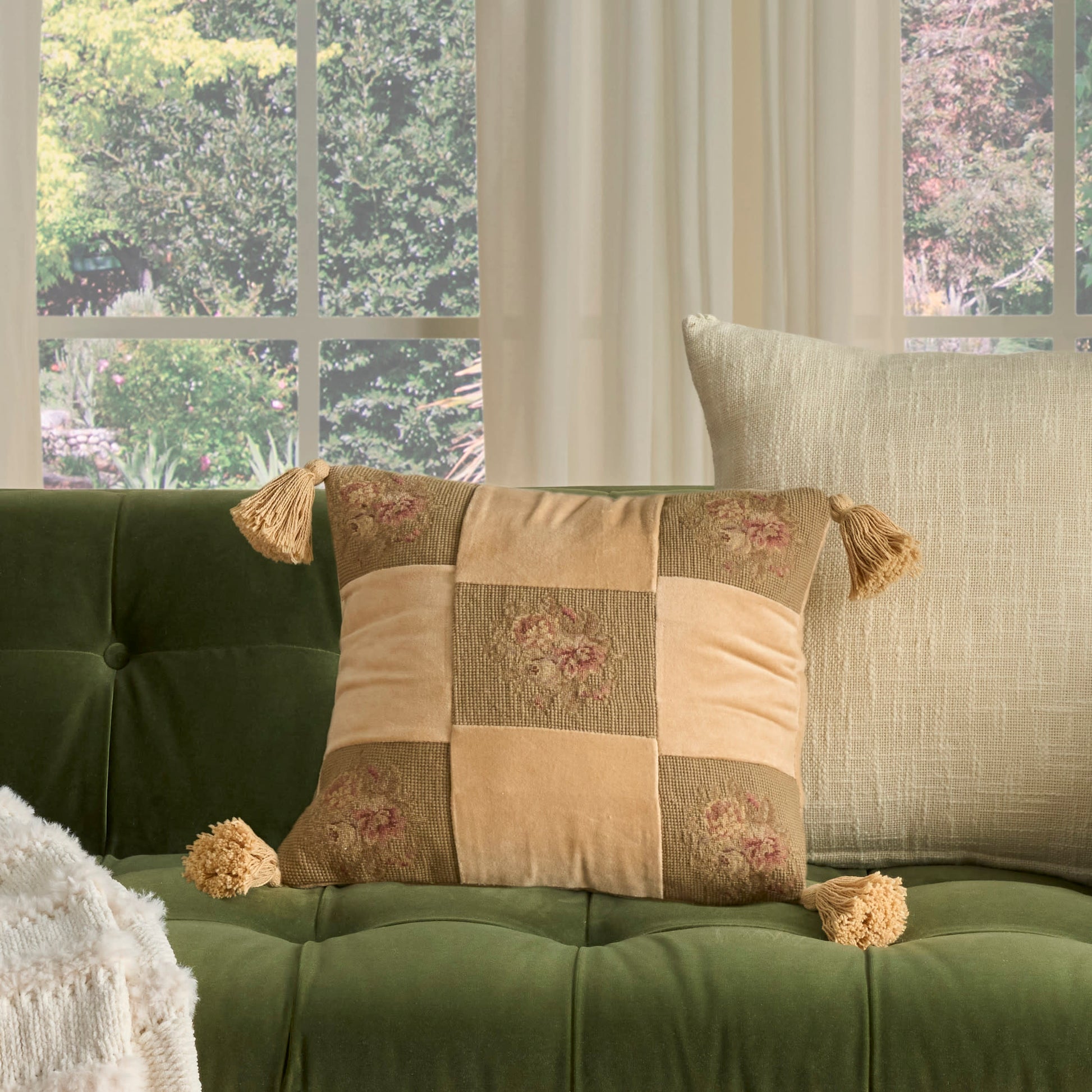 Olive green decorative pillow with vintage pattern on a sofa, paired with a cream cushion.