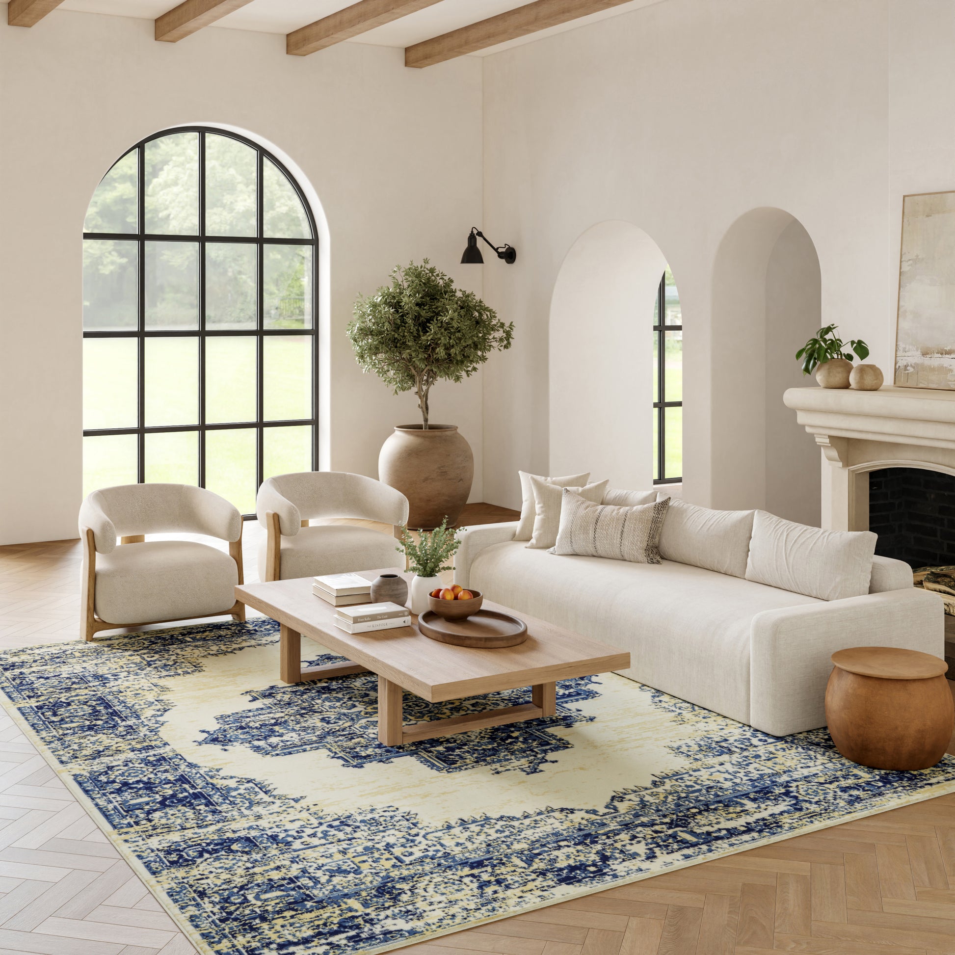 Neutral living room with arched window, beige sofa and armchairs, wooden coffee table, blue rug, potted tree, fireplace.