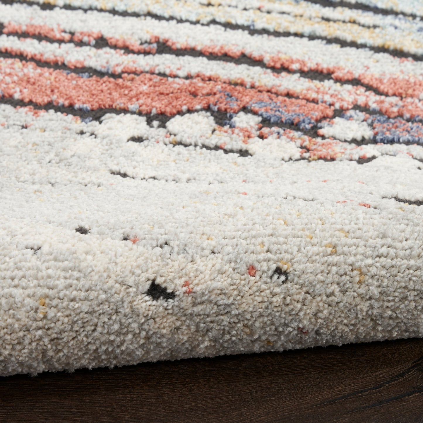 Textured shag rug with cream, peach, coral and blue stripes on dark wood floor.