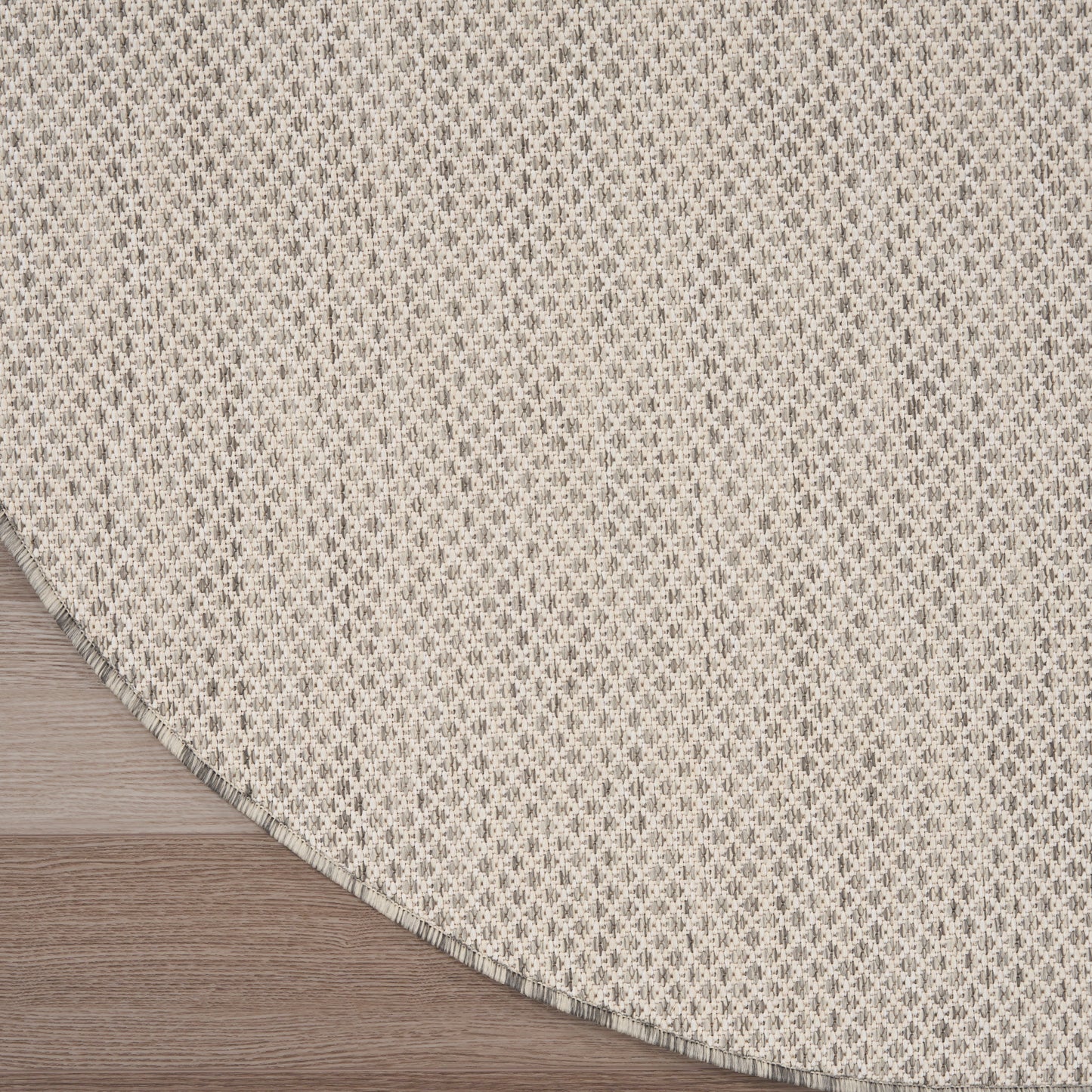 Beige round woven rug with tiny gray geometric pattern; textured textile on wood floor.