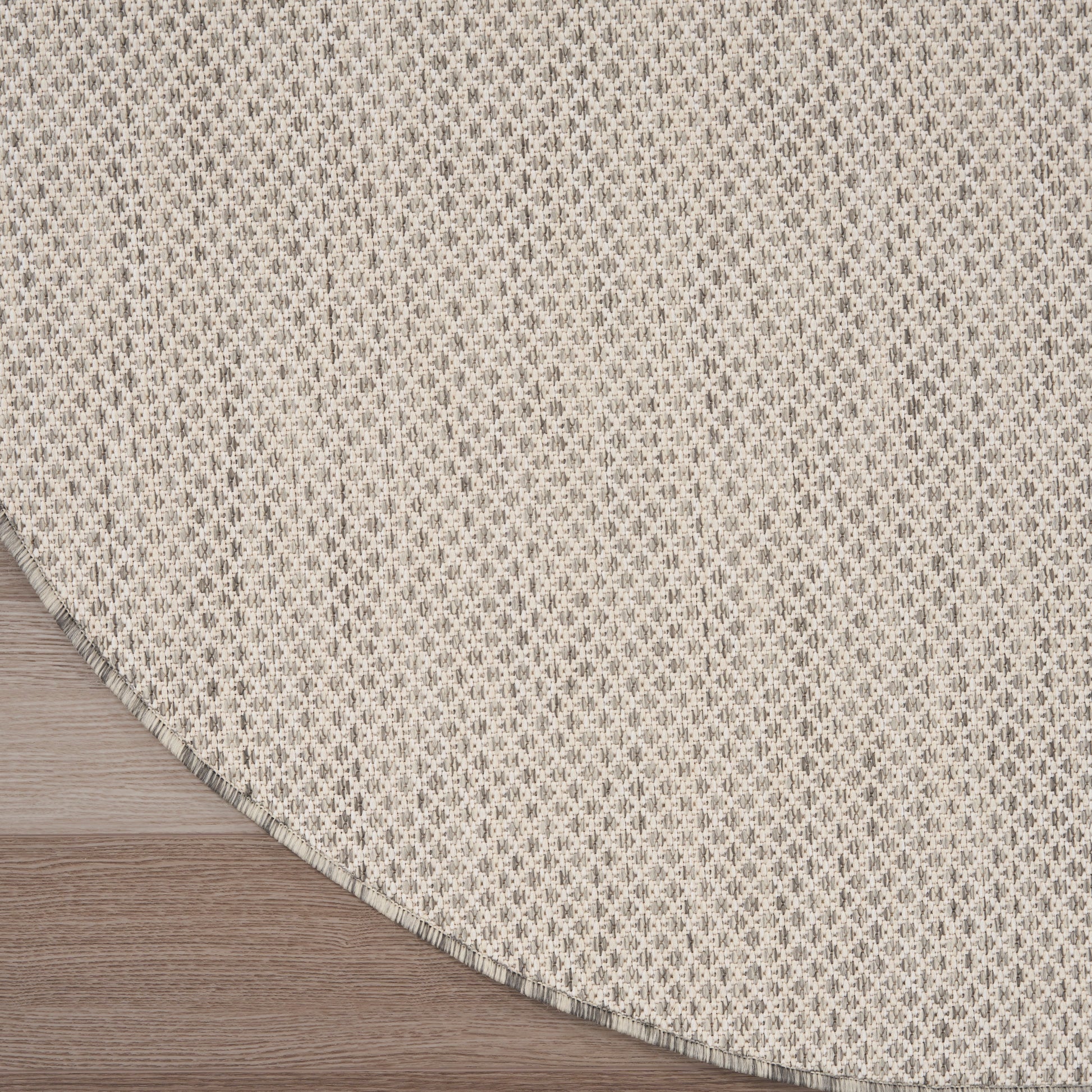 Beige round woven rug with tiny gray geometric pattern; textured textile on wood floor.