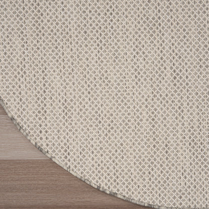 Beige round woven rug with tiny gray geometric pattern; textured textile on wood floor.