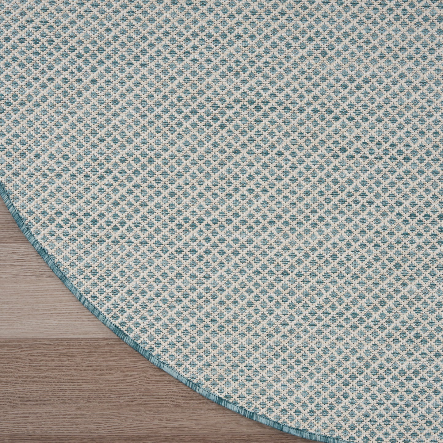 Round woven rug with teal and cream diamond lattice pattern and teal border on a wooden floor.