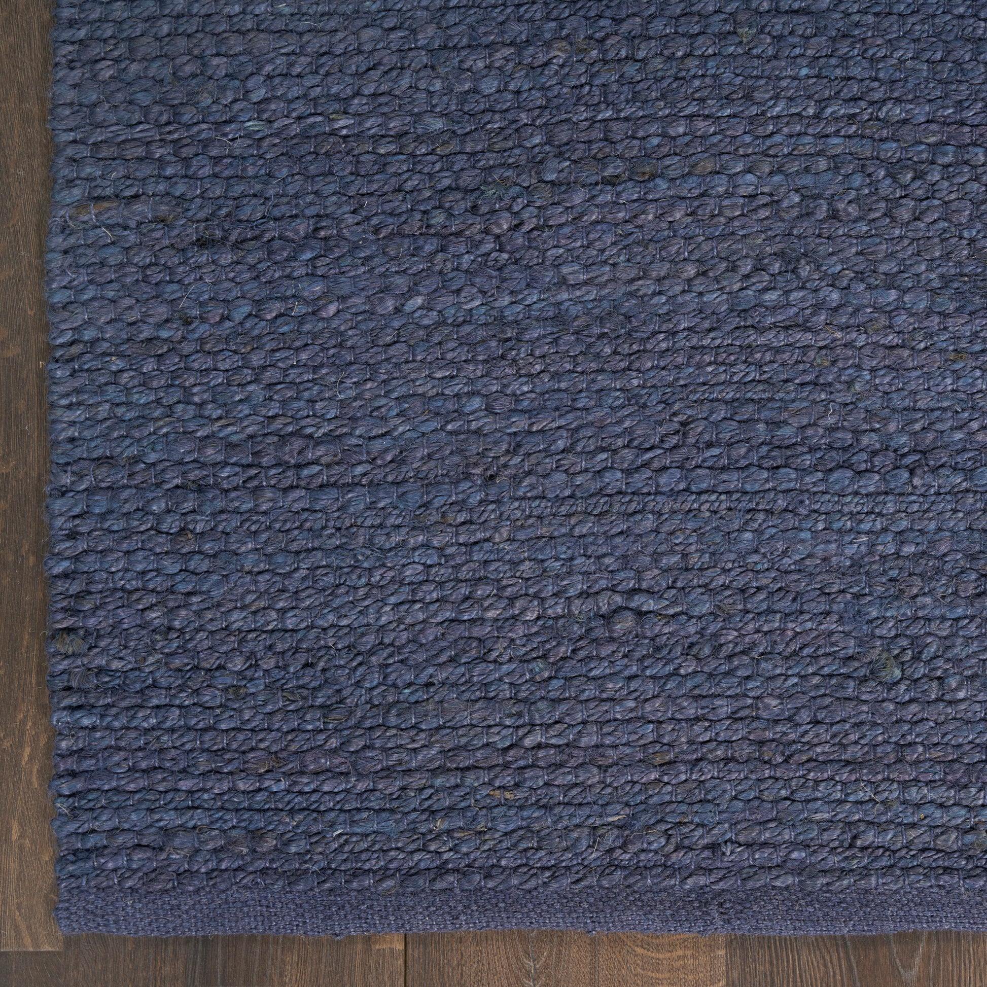 Blue loop-pile rug with a darker navy border on wood floor; dense textured weave for living areas.