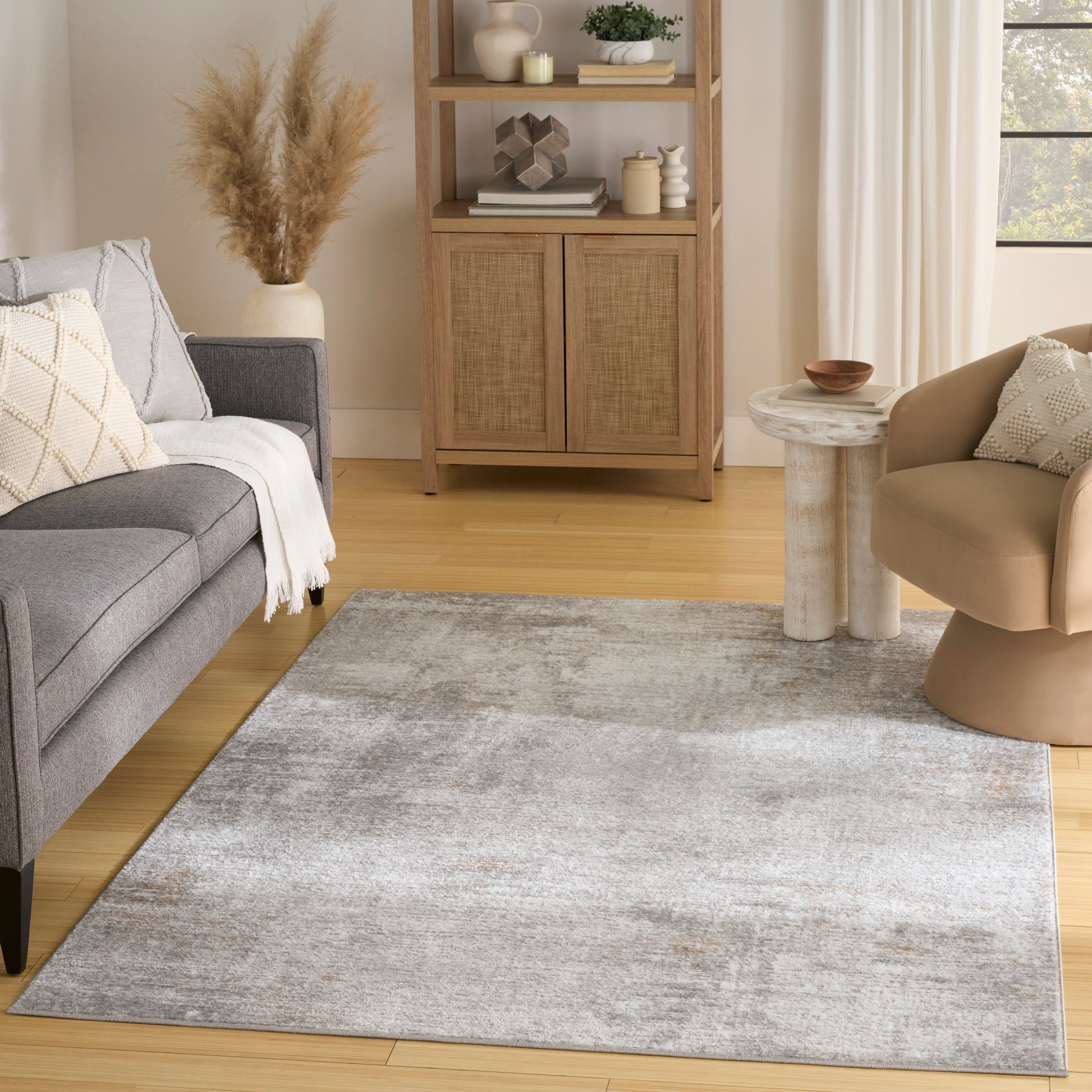 Neutral living room with light gray abstract rug, gray sofa with cream throw, beige armchair, woven cabinet, pampas grass vase.