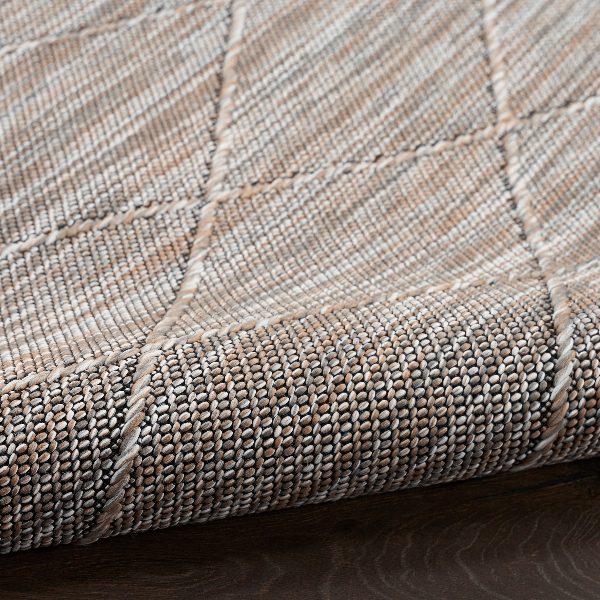 Close-up of beige-gray patchwork woven rug with grid seams and textured looped pile, perfect for living room floors.