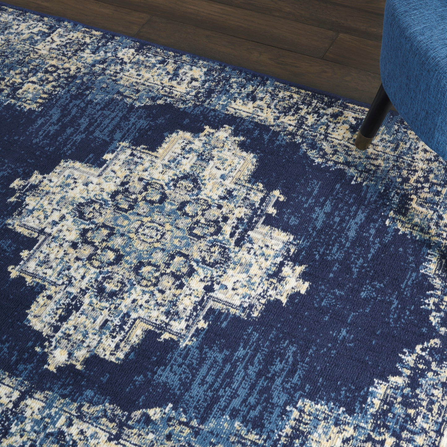 Blue vintage oriental rug with ivory medallion, distressed pattern on dark wood floor beside a blue upholstered chair.