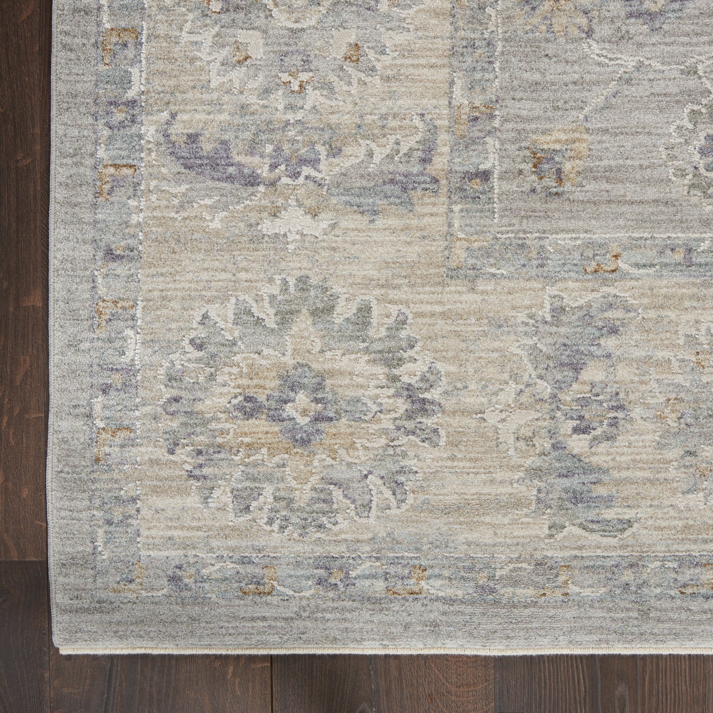 Muted oriental rug with blue, lavender, beige & gray floral medallions and decorative border on dark wood floor.
