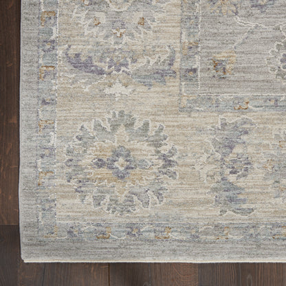Muted oriental rug with blue, lavender, beige & gray floral medallions and decorative border on dark wood floor.