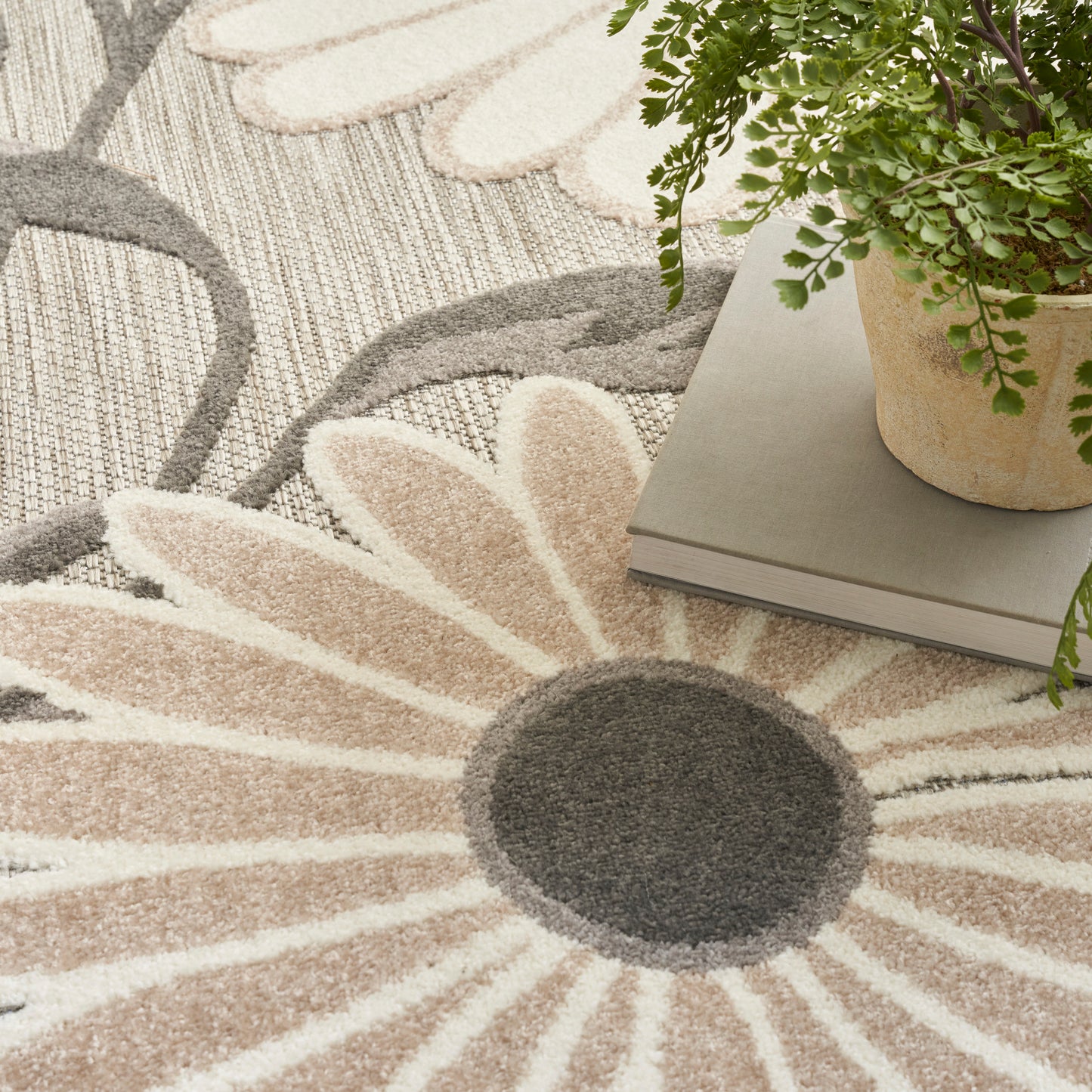 Beige and cream sunburst floral rug with a dark gray center; plant and books rest on top.