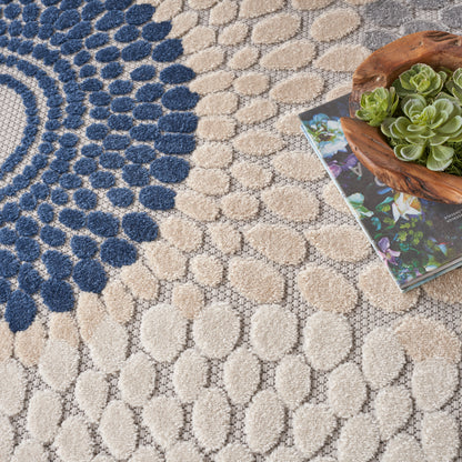 Beige circular pebble-pattern rug with navy blue spiral clusters; wooden planter with succulents atop a colorful magazine.