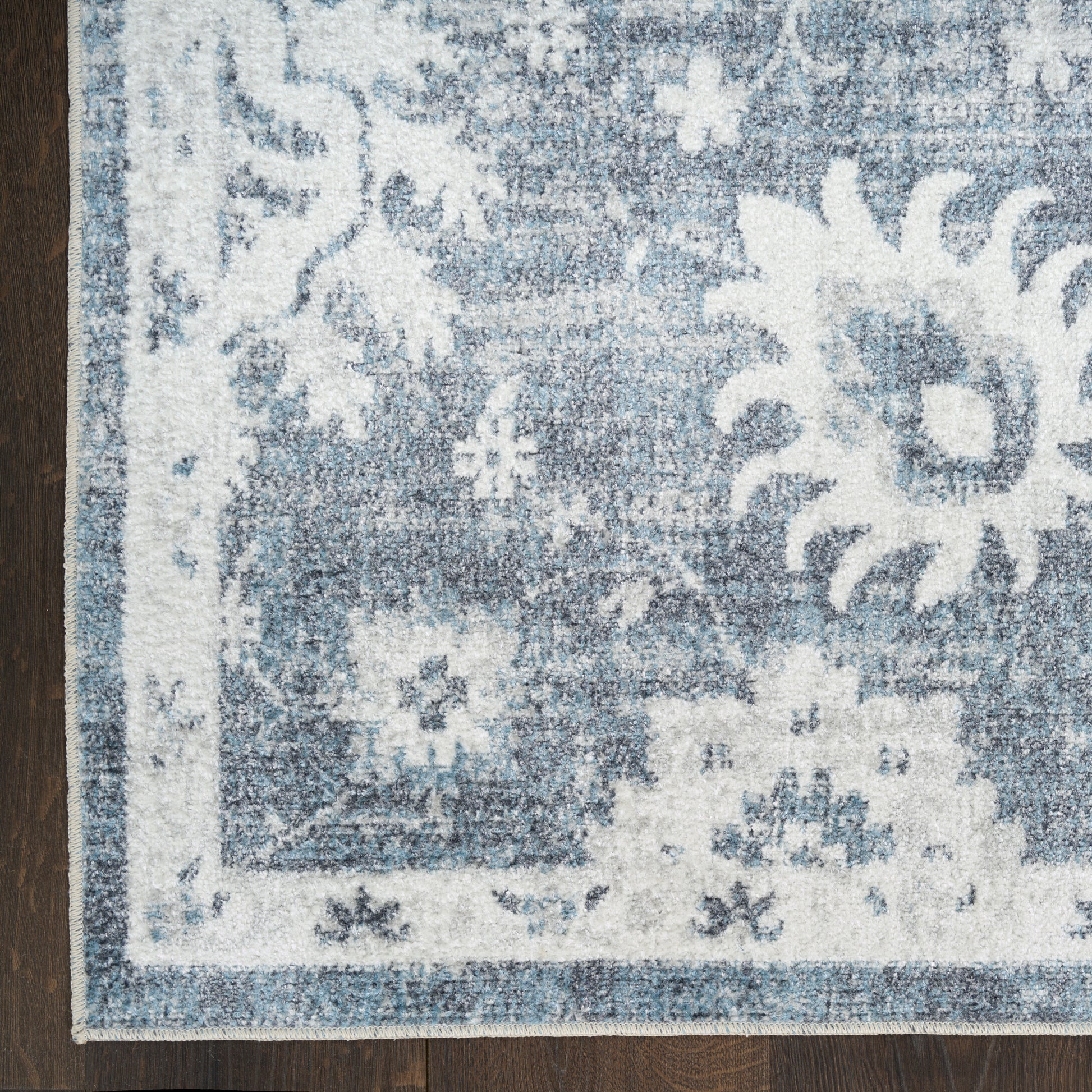 Blue and white distressed floral medallion area rug on dark wood floor.