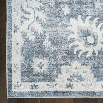 Blue and white distressed floral medallion area rug on dark wood floor.