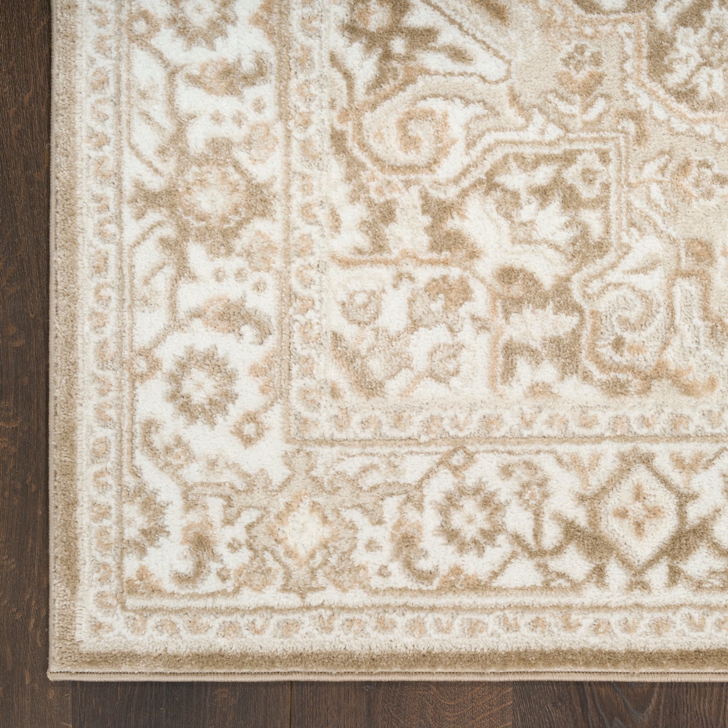 Cream and tan oriental-style area rug with floral motifs and decorative border on dark wooden floor.