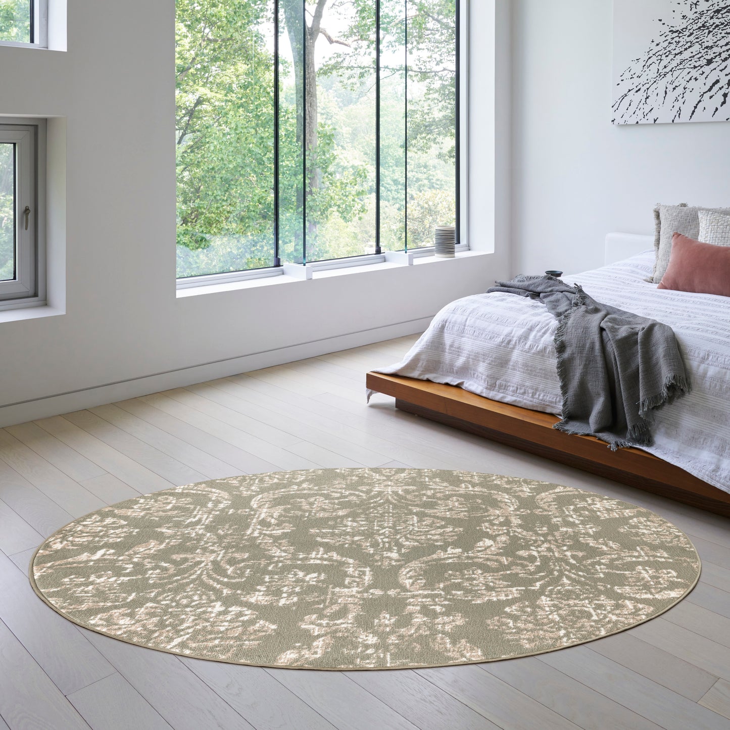 Round 8' beige area rug with subtle damask pattern in a bright modern bedroom beside a low wooden platform bed.