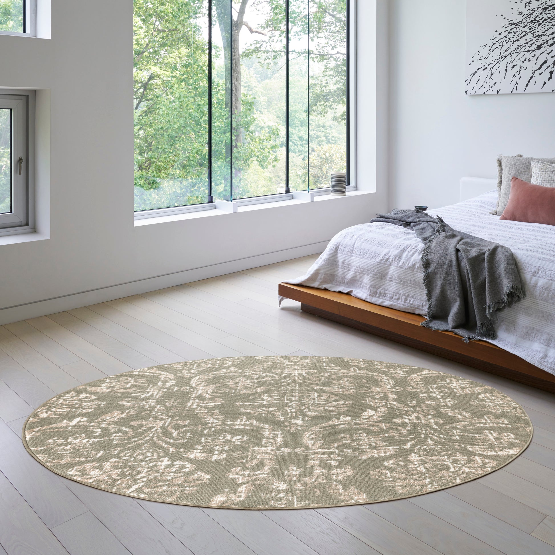 Round 8' beige area rug with subtle damask pattern in a bright modern bedroom beside a low wooden platform bed.