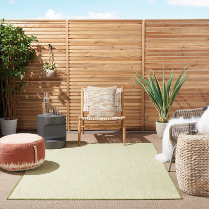 Sunny outdoor patio with wooden slat fence, beige woven chair, olive rug, orange pouf, and potted plants.