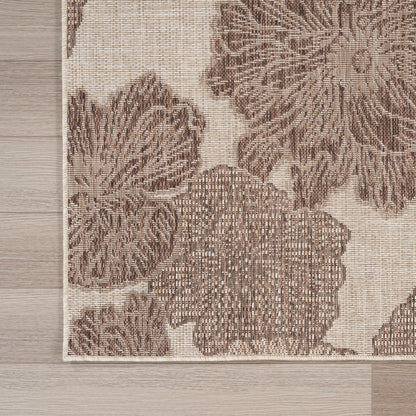 Beige area rug with tropical pattern, woven texture and light border on a wooden floor.